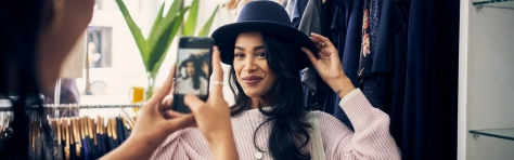 Retail technology - woman trying on hat while friend takes picture with cell phone
